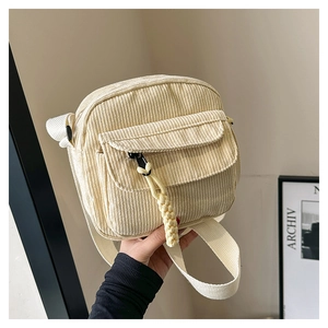 Detail of beige corduroy crossbody bag texture with woven zipper pendant and front pocket