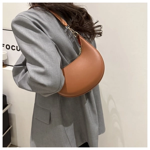 Detail view of a caramel crescent leather shoulder bag worn by a model in a grey blazer
