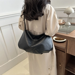 Large black pleated hobo shoulder bag in soft faux leather shown in a lifestyle cafe setting
