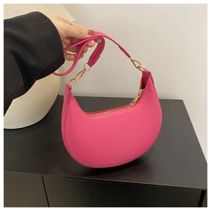 Detailed close-up of hot pink crescent leather handbag with gold metal hardware