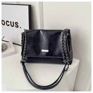 Detailed close-up of dark blue glossy shoulder bag with silver chain and logo plaque