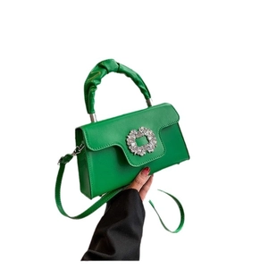 Green faux leather crossbody bag with crystal buckle and ruched handle on white backdrop