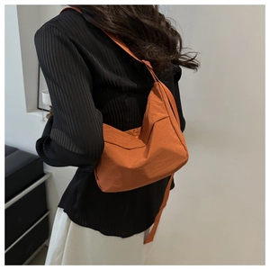 Detail view of large orange nylon tote bag worn crossbody on casual striped shirt
