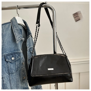 Detail of a black leather handbag with silver chain strap against a denim jacket