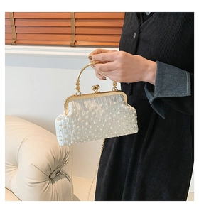 Close-up of elegant white pearl evening bag with gold handle and satin pleats