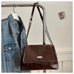 Detail of dark brown glossy shoulder bag with silver chain strap on a denim jacket