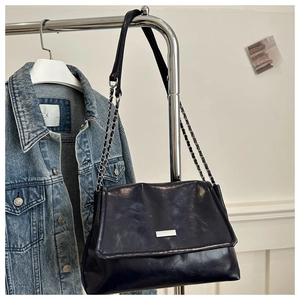 Close-up of black glossy oil wax leather shoulder bag with silver chain strap and metal logo