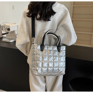Macro shot of silver quilted puffer tote bag with black strap and metallic texture