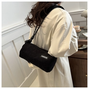 Close-up of black corduroy cylinder bag featuring a white FASHION tag and woven strap