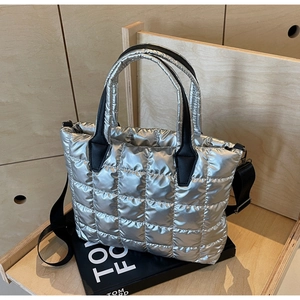 Detail of silver quilted puffer tote bag with black leather handles on display