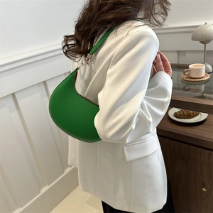 Elegant emerald green crescent hobo bag with gold hardware worn by model in white suit