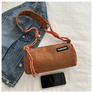 Close-up of brown corduroy cylinder bag with FASHION patch and braided shoulder strap