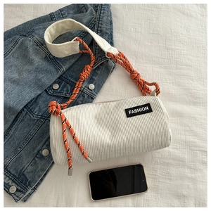Detail of white corduroy crossbody bag with orange woven strap and fashion label