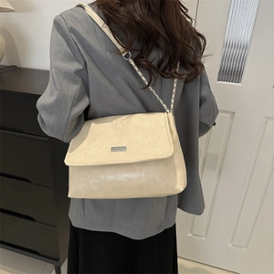 Minimalist cream beige chain shoulder bag with metal logo in a lifestyle commute setting