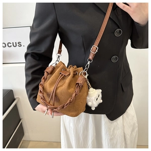 Detailed shot of brown suede bucket bag with woven handle and plush toy charm