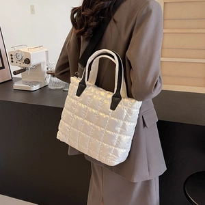 Quilted white puffer tote bag with black straps worn by a model in a cafe setting