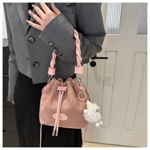 Pink faux suede bucket bag with woven handle and plush charm detail on a model