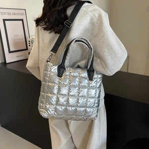 Silver quilted puffer tote bag with black straps worn by a model in a minimalist room