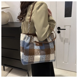 Detail of wool plaid tote bag with brown leather straps and metal chain accents