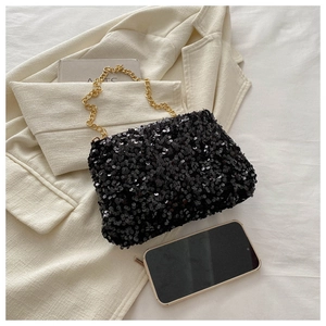 Close-up of black sequin handbag with a heavy gold chain handle on a beige blazer background