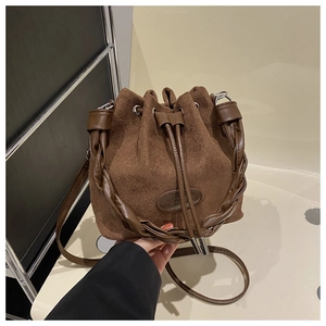 Macro detail of brown suede bucket bag with woven handle and drawstring closure