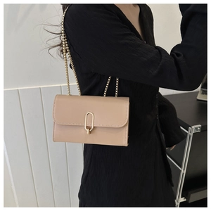 Detail of beige square chain bag with gold oval clasp and smooth finish on black top