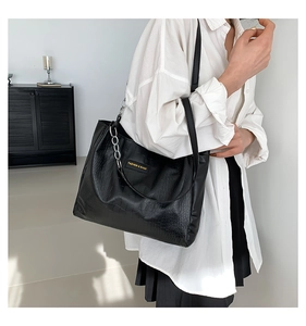 Close-up of black crocodile pattern tote bag with silver chain and metal brand plate