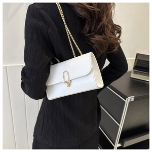 Detail of white glossy flap bag with golden oval clasp and fine chain strap
