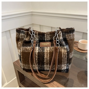 Detail of wool plaid tote bag featuring brown leather straps and silver metal chain links