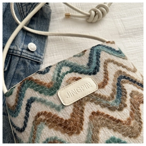 Detail of wave pattern woven bag with leather brand logo and metal buckle on denim