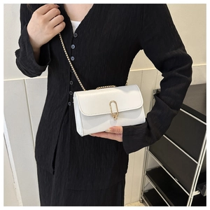 White leather square bag with gold oval lock and chain strap shown on model's shoulder