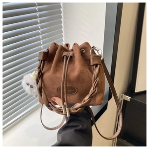 Detail of brown suede bucket bag with woven handle, drawstring closure and plush pendant