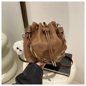 Close-up of brown suede bucket bag with woven handle and plush charm detail