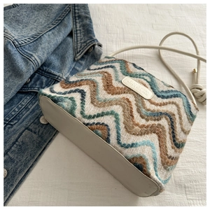 Detailed close-up of colorful crochet knit shoulder bag with blue wave pattern and leather tag