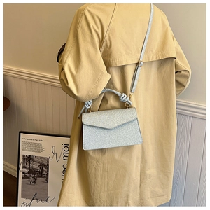 Detail of light blue sequined envelope bag with knotted handle on a model in beige coat