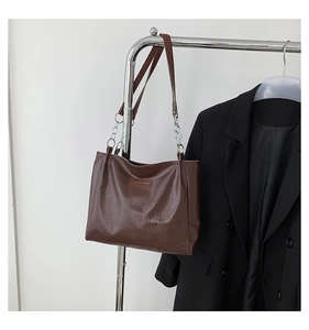 Macro detail of dark brown crocodile embossed leather tote bag with metal chain strap