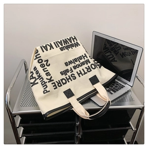 Detail view of large canvas tote bag with letter print and black leather handles