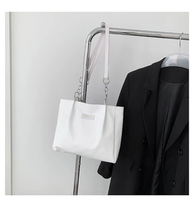 Close-up of white leather tote bag featuring silver chain straps and brand label
