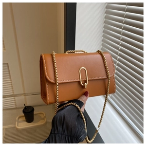 Close-up of tan leather crossbody bag featuring gold chain and white contrast stitching