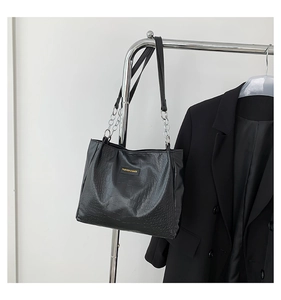 Detail of black faux leather tote bag with crocodile pattern and silver chain strap