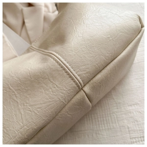 Close-up of textured cream faux leather tote bag showing high-quality stitching detail