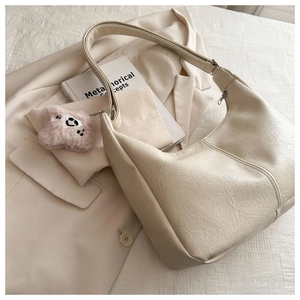 Detail of beige hobo bag with litchi texture and pink plush bear pendant accessory