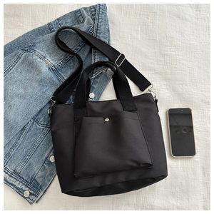 Detail of black nylon tote bag with front snap pocket and adjustable strap on denim