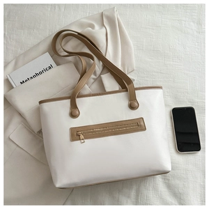 Detail view of cream leather tote bag with brown trim and golden zipper pocket