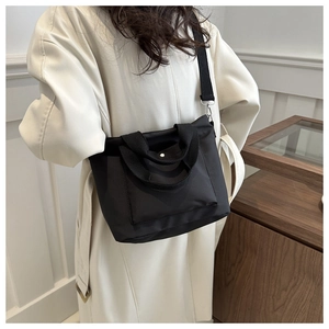 Versatile black nylon tote bag worn crossbody with adjustable shoulder strap and metal buckle