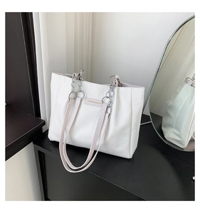 Close-up of white tote bag with crocodile pattern and chain strap on black stand