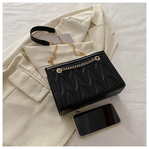 Detail of black quilted shoulder bag with V-shaped wave stitching and gold chain