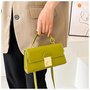 Detail of avocado green leather handbag with golden lock and circular handle on model