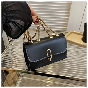 Detail of black leather crossbody bag with white stitching and golden chain strap