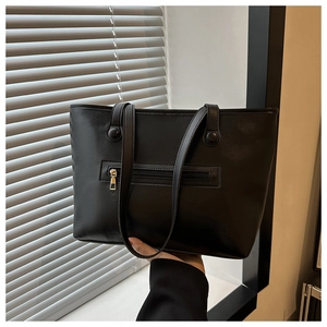 Detail shot of the back zipper pocket on a black leather tote bag with gold metal hardware